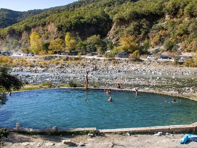 Personas nadando en una piscina natural circular de aguas termales junto a un río.