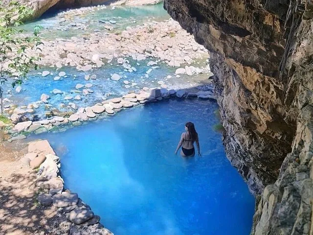 Mujer en bikini negro de pie en una piscina natural azul cerca de un río.