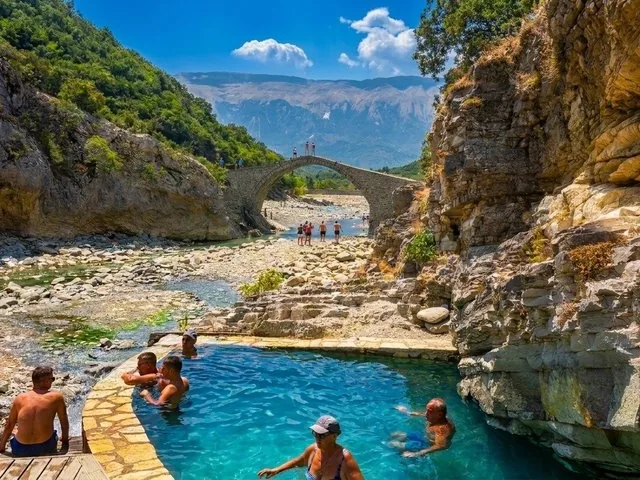 Menschen beim Schwimmen in einer natürlichen Thermalquelle nahe einer Steinbrücke.