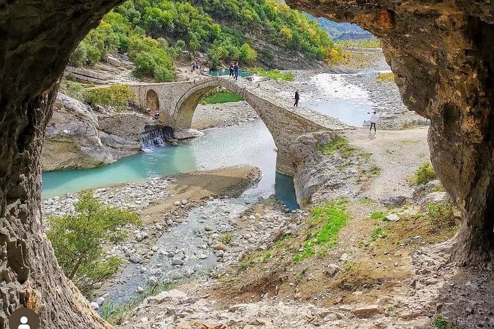 Blick aus einer Höhle auf eine Steinbrücke über einen Fluss.