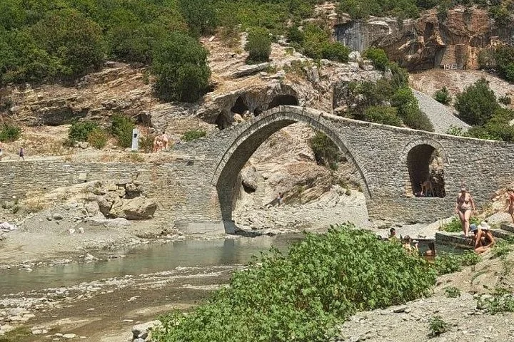 Steinbrücke über einen Fluss mit badenden und umhergehenden Menschen.